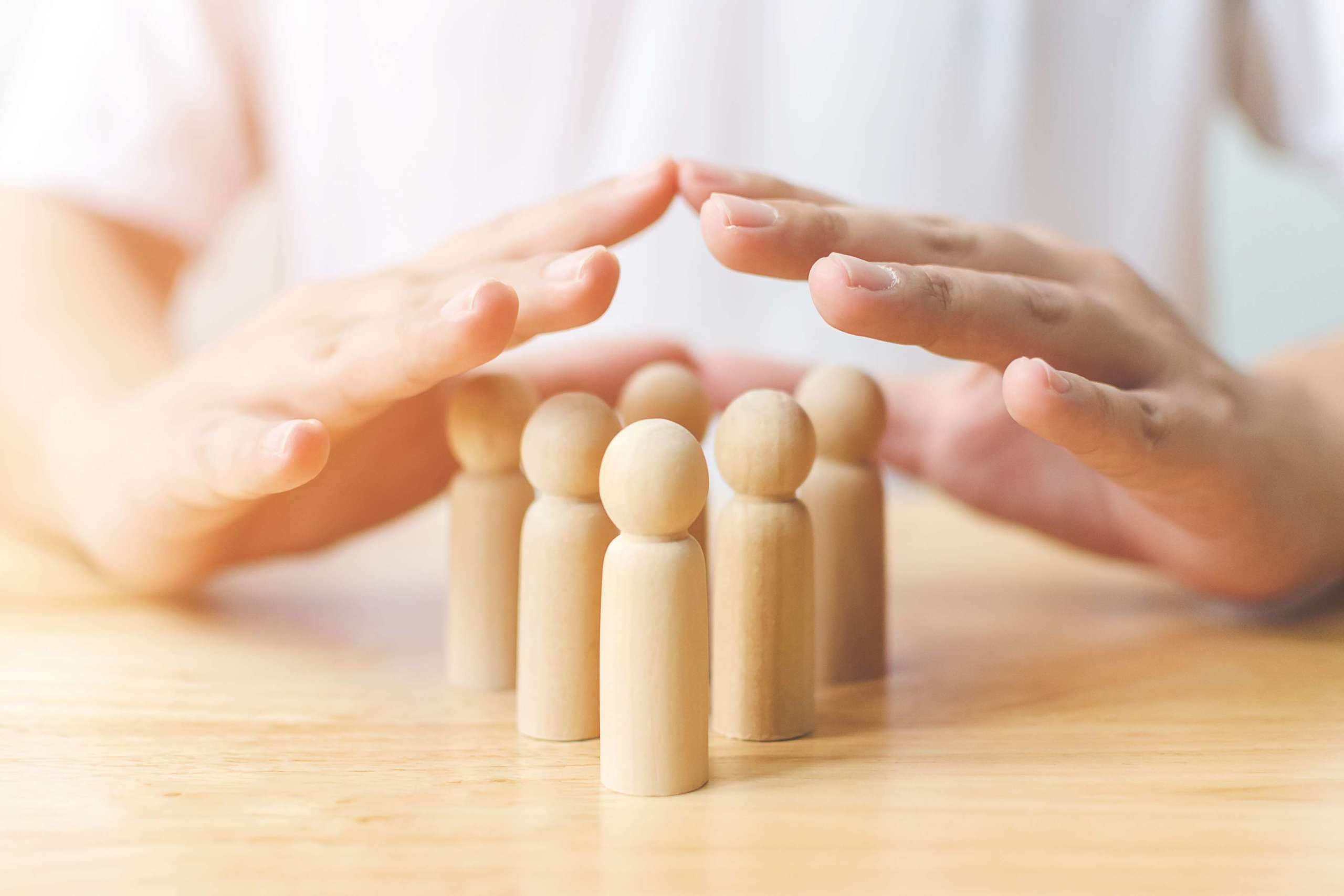 Schutz der Menschen Gesundheit und Versicherungskonzept. Handschild schützt hölzernen Menschen auf dem Tisch