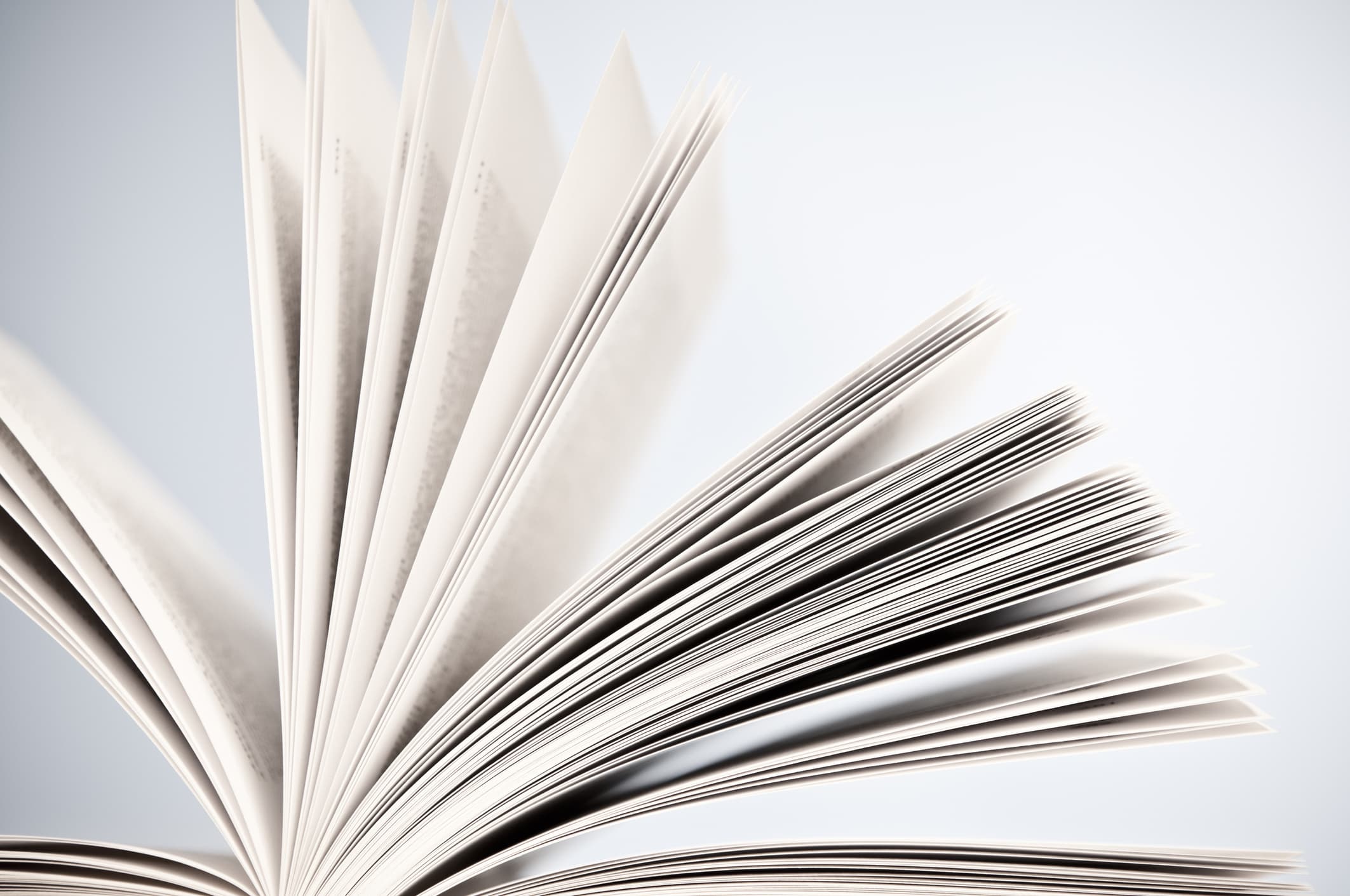 Ein offenes Buch, Seiten durchblätternd, hellblauer Hintergrund. Horizontal, Studioaufnahme.
