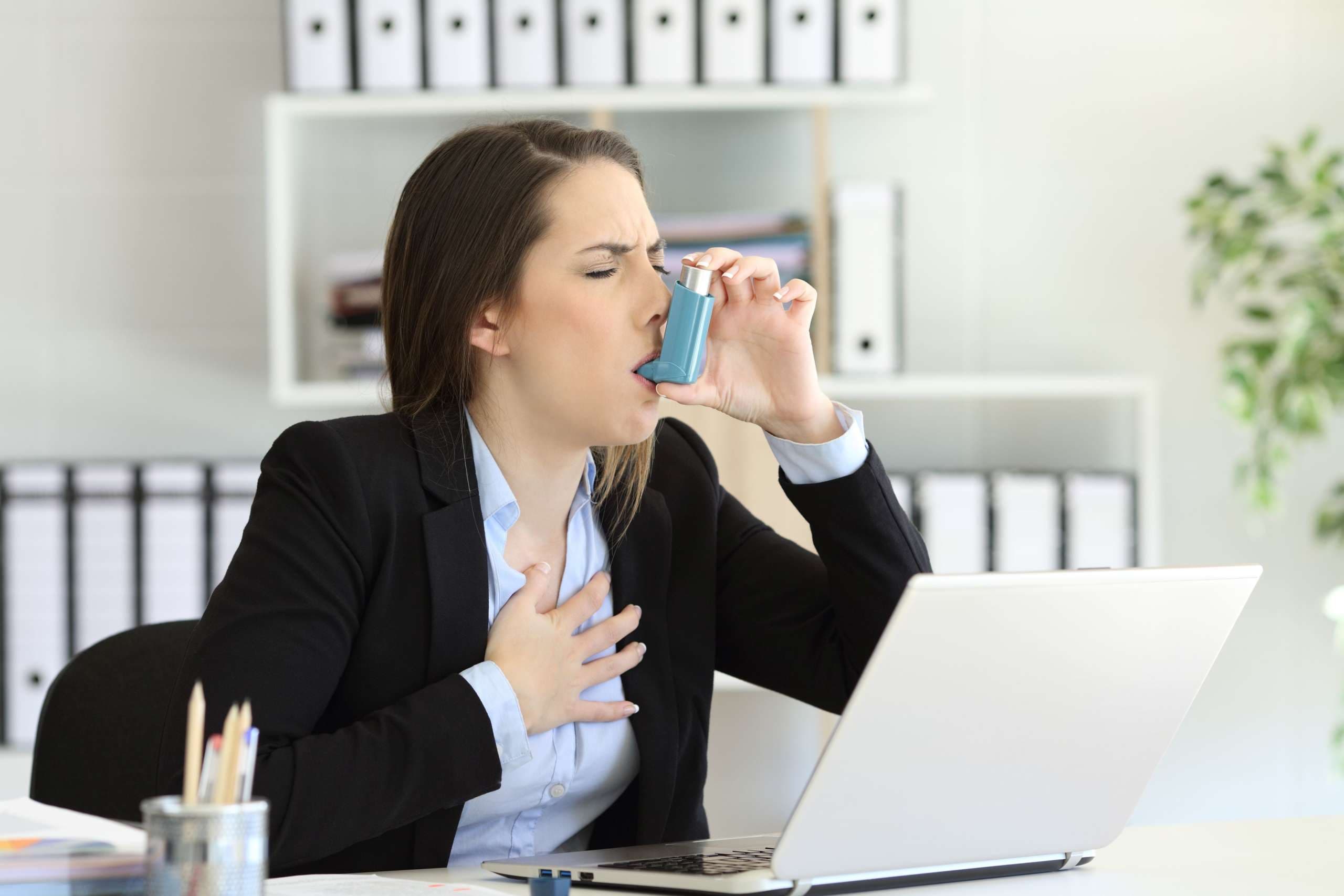 Asmathische Führungskraft mit einem Asthmaanfall, der im Büro mit einem Inhalator inhaliert