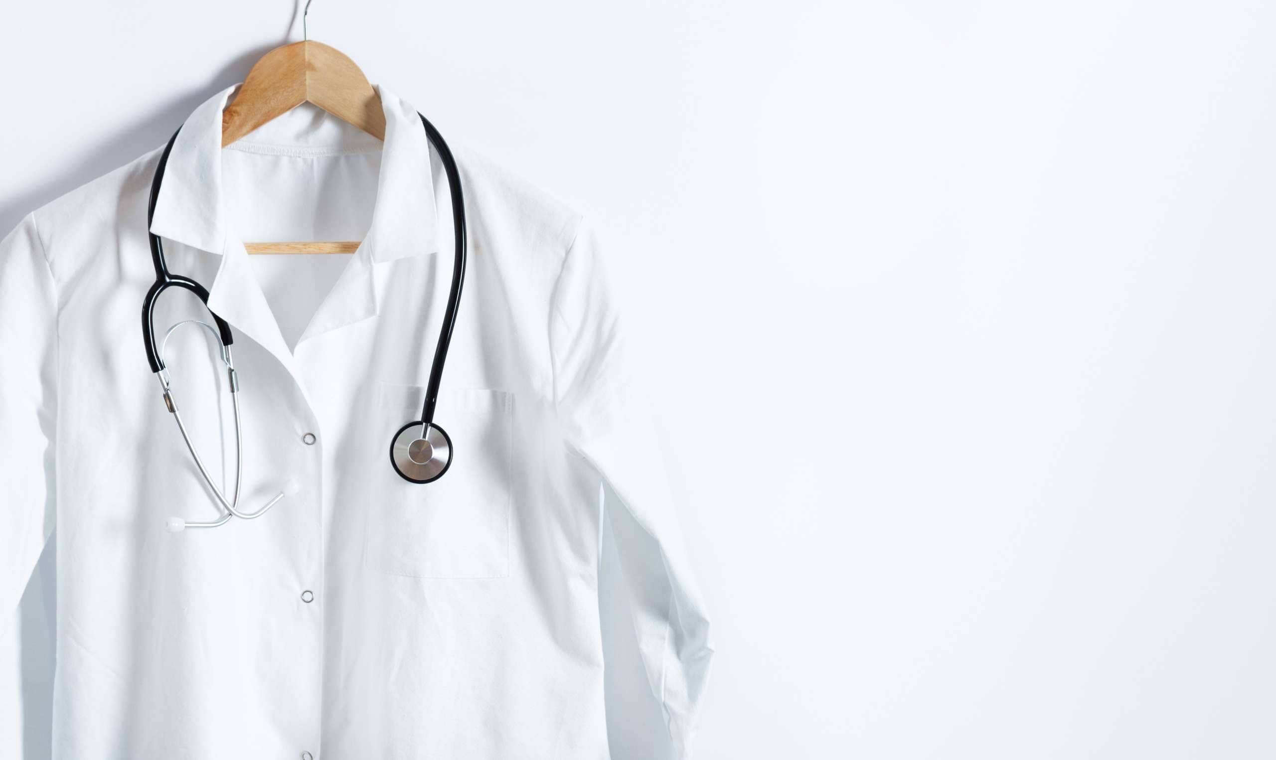 Weißer Kittel des Doktors mit Stethoskop auf Aufhänger über weißem Hintergrund mit Kopienraum. Gesundheitswesen und medizinisches Konzept.