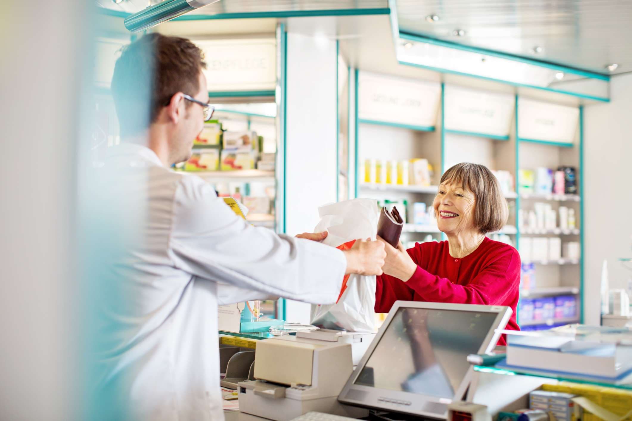 Männlicher Apotheker gibt älteren Kunden in einer Apotheke verschreibungspflichtige Medikamente