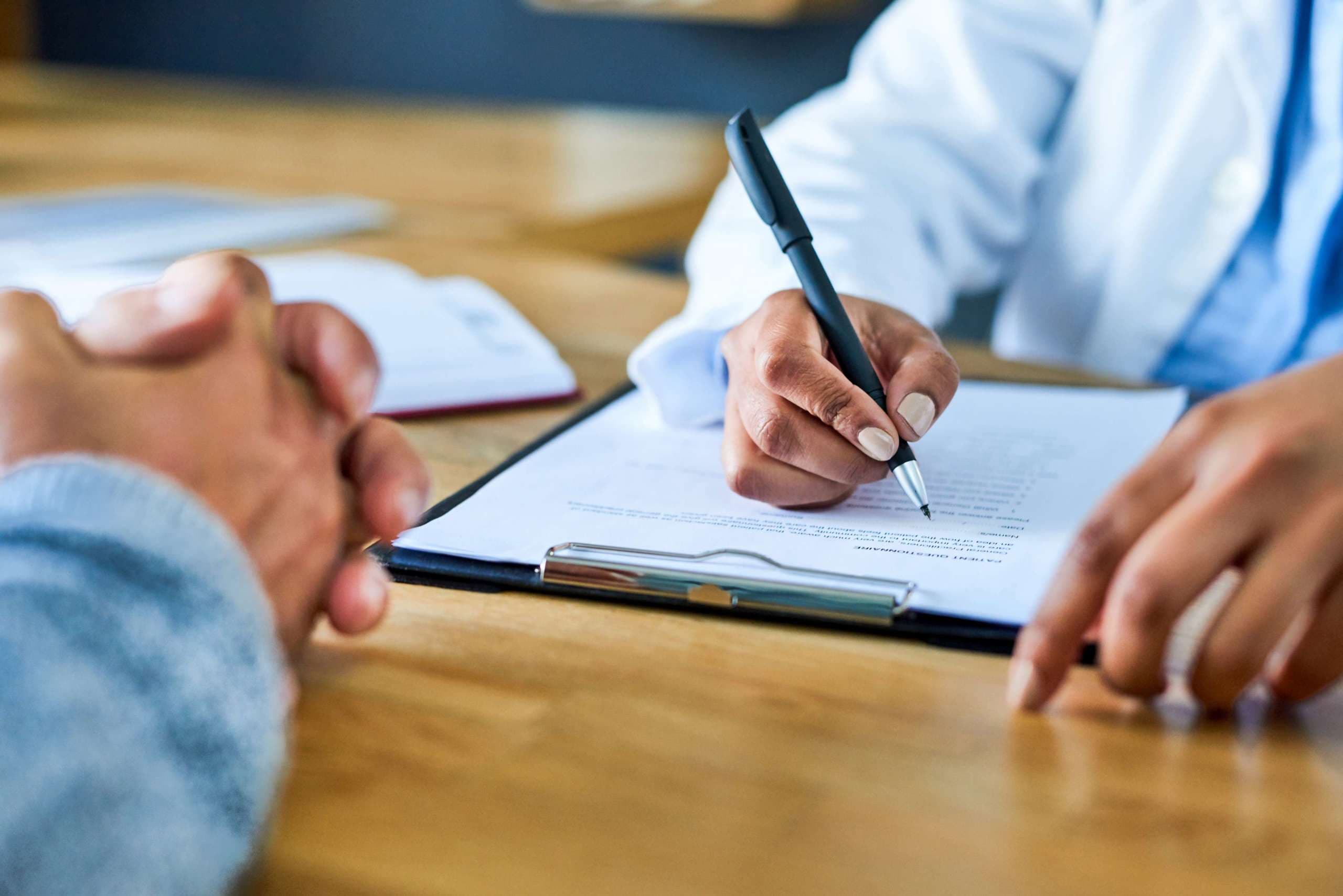 Nahaufnahme eines Arztes, der während einer Konsultation mit einem Patienten Notizen schreibt