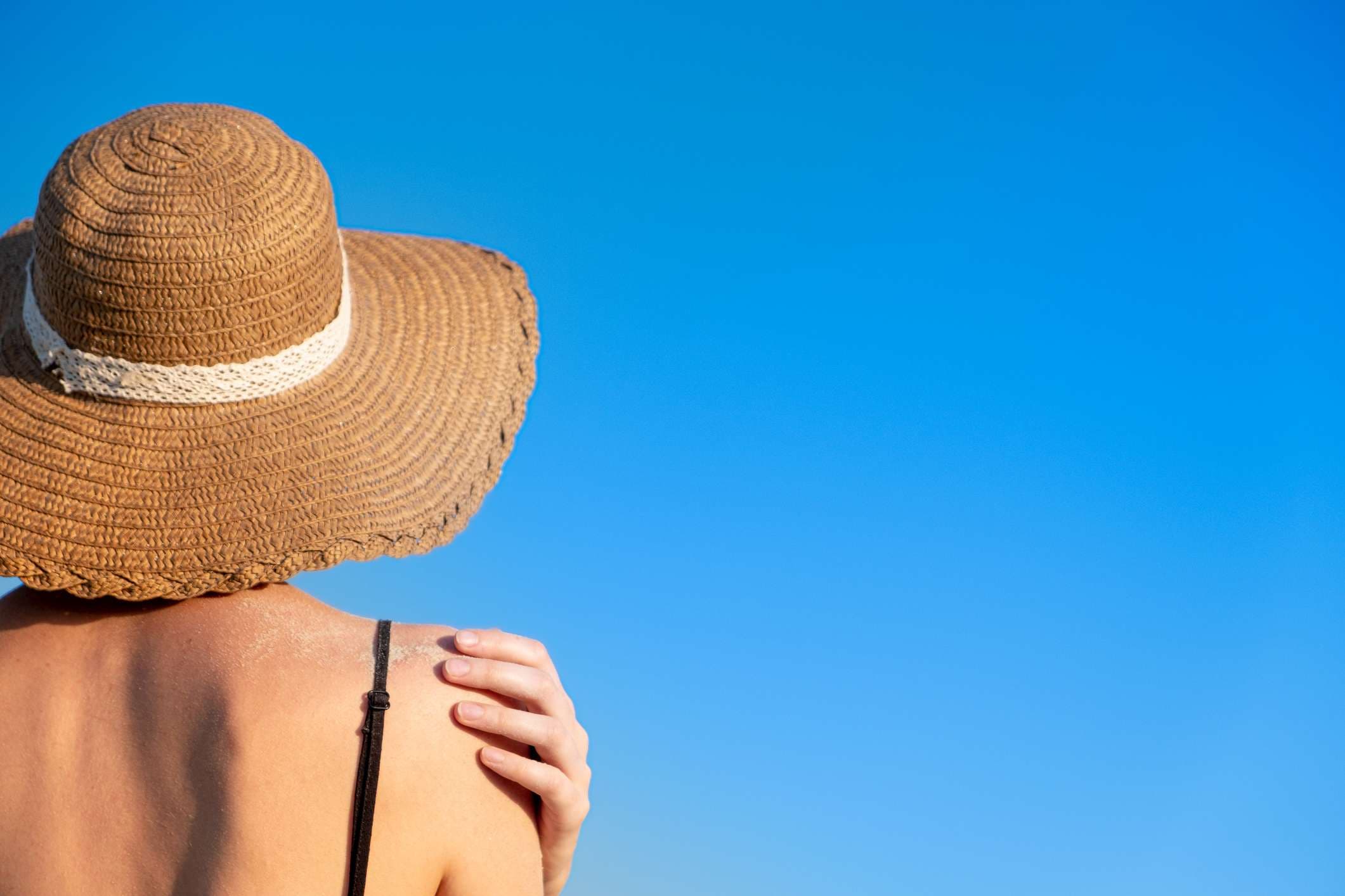 Sommerferienstimmung: Frau mit Strandhut, bedeckt mit Sand auf hellblauem Hintergrund.