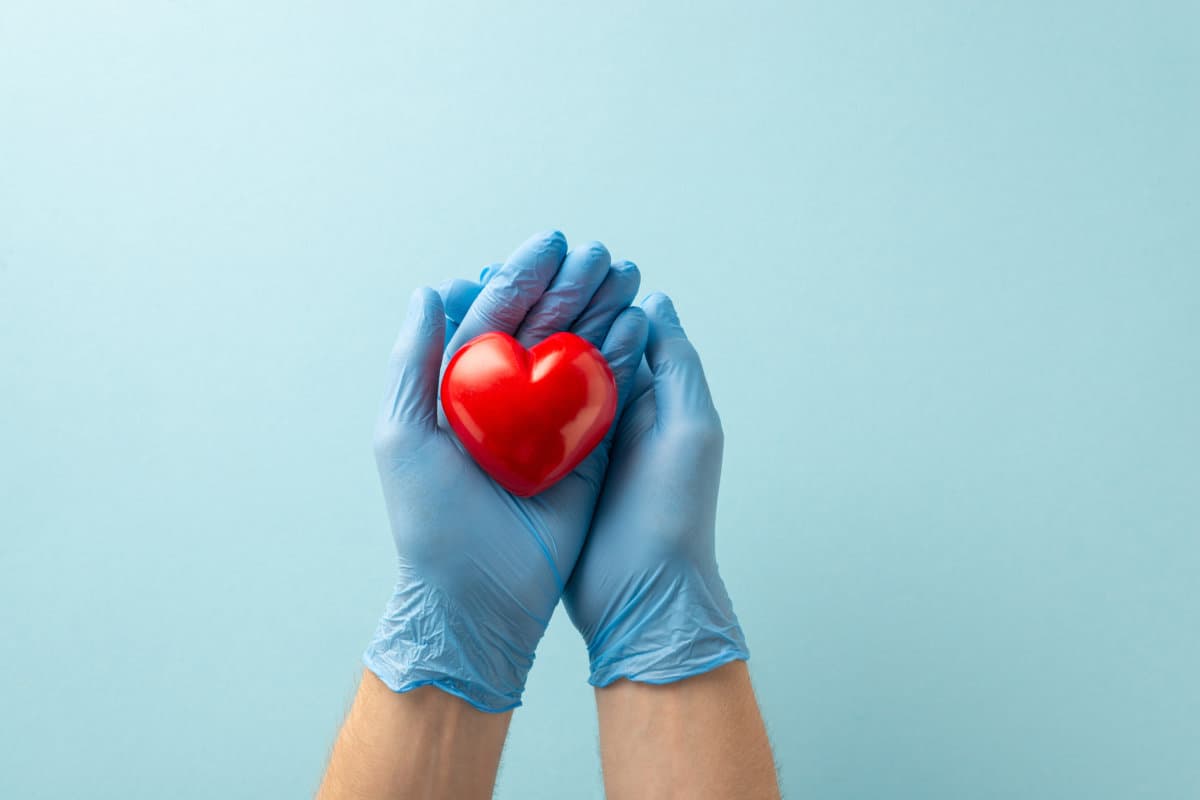 Heart disease prevention concept. Top view photograph of hands in medical gloves holding a heart model on light blue isolated background with copy-space for text or advertising placement