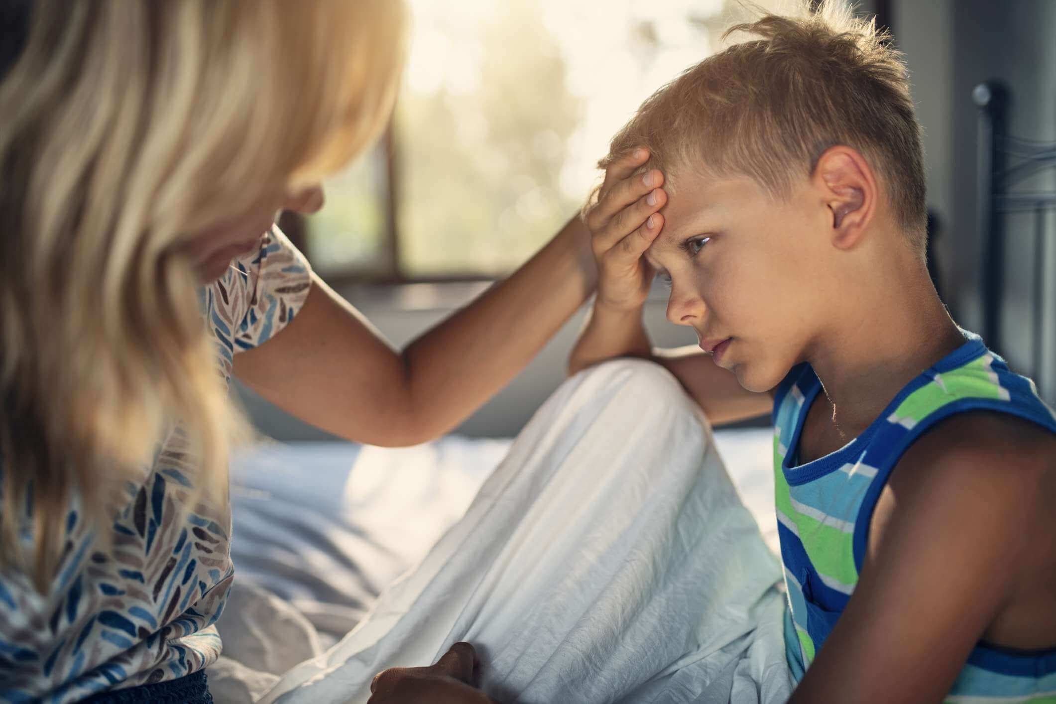 Kranker kleiner Junge, der auf dem Bett sitzt. Der Junge hat Kopfschmerzen und Fieber.
Die Mutter tröstet den Jungen.
Nikon D850