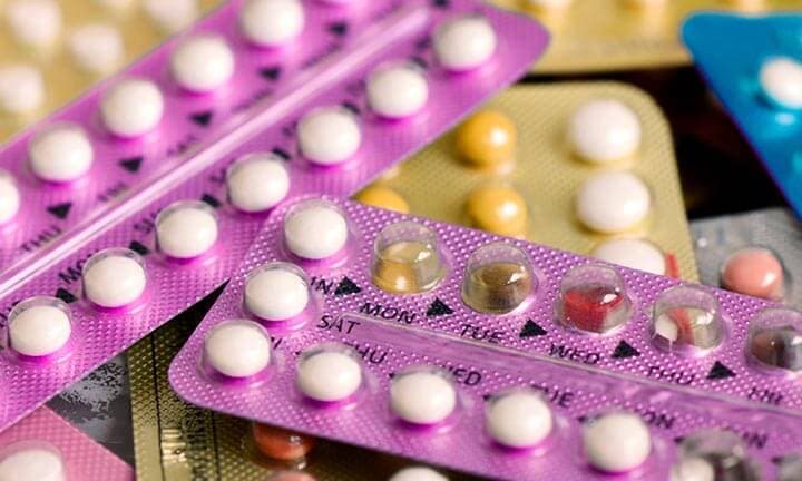 Oral contraceptive pill on pharmacy counter with colorful pills strips background.