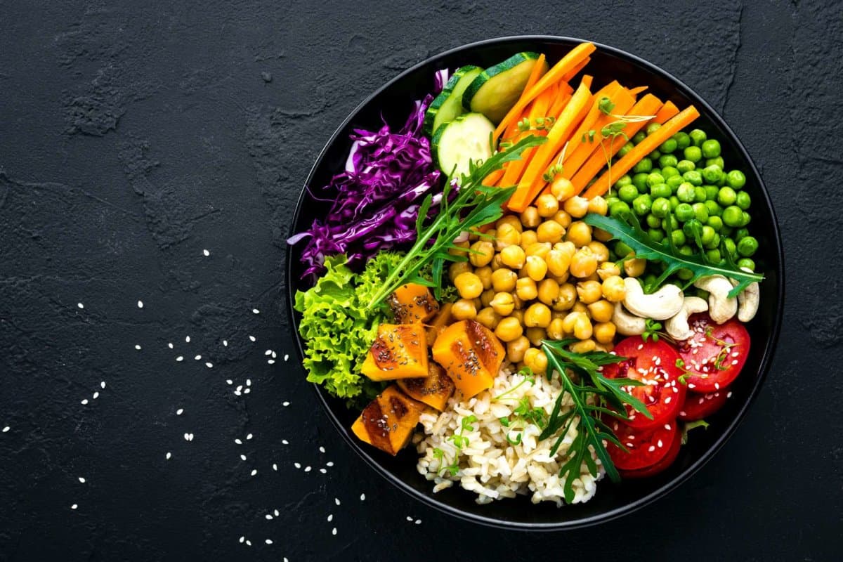 Schüsselgericht mit Naturreis, Gurken, Tomaten, grünen Erbsen, Rotkohl, Kichererbsen, frischem Kopfsalat und Cashewnüssen. Gesunde ausgewogene Ernährung