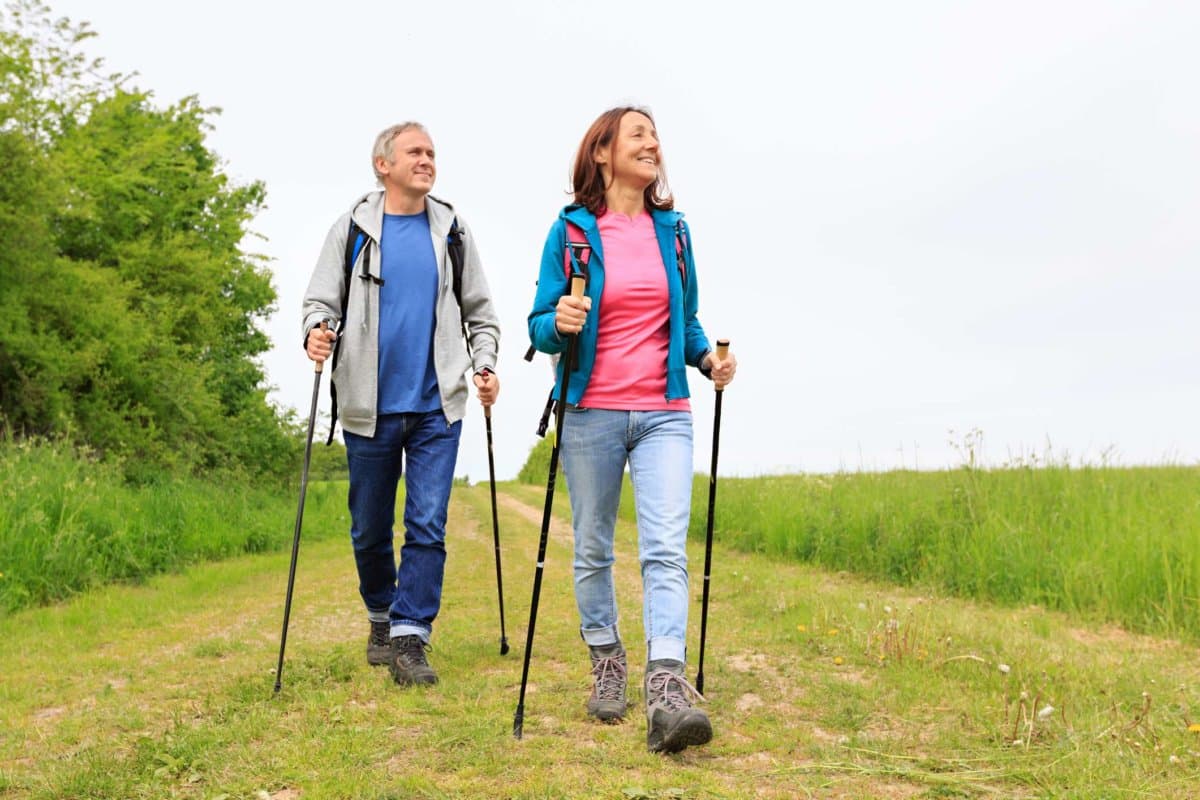 Nordic Walking - aktives älteres Paar genießt einen Spaziergang durch die grüne Natur