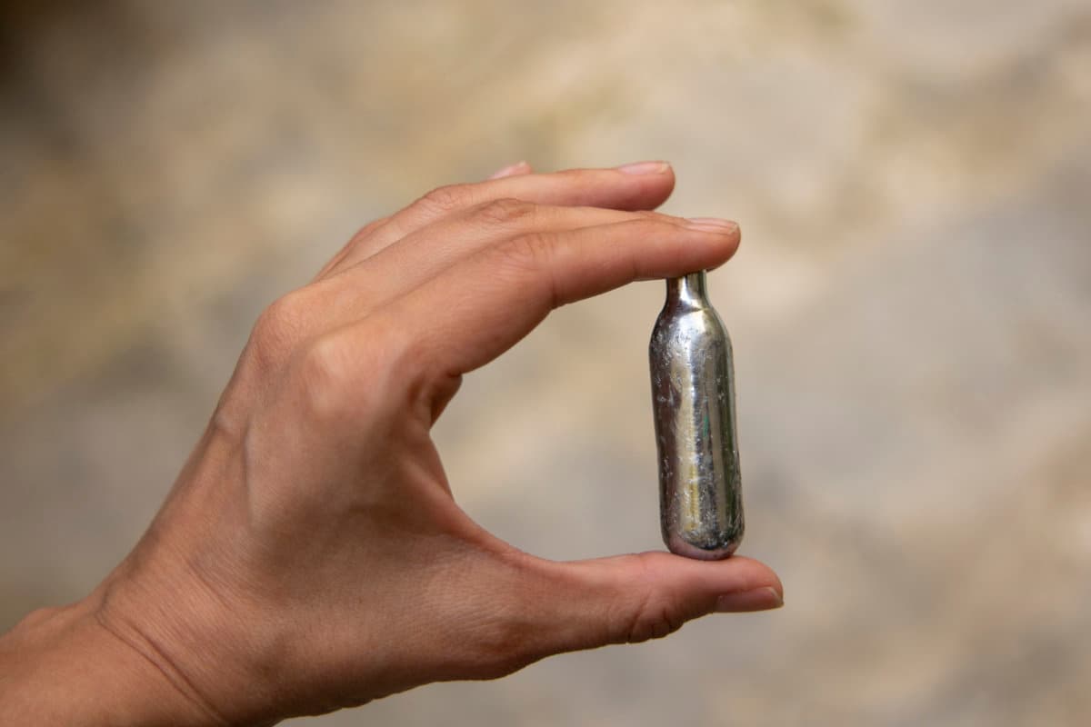 Er hält ein kleines Fläschchen mit Lachgas in der Hand, das bei jungen Menschen als Droge und Lachgas verwendet wird