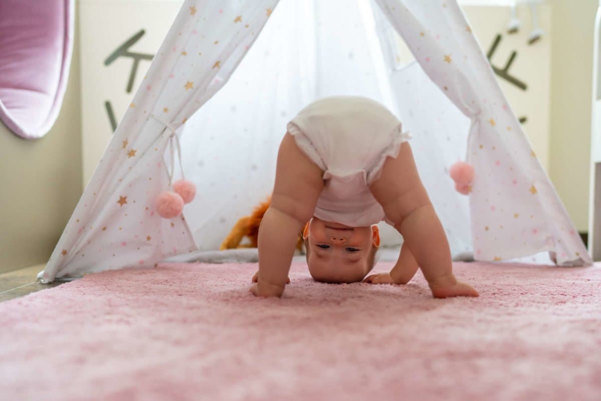 Niedliches kleines Mädchen, das kopfüber auf dem Teppich im Schlafzimmer steht