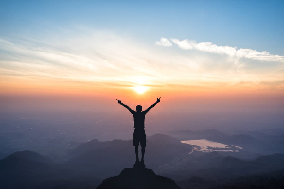 Silhouette of man spreading hand and enjoy great sunrise above the mountain valley and morning mist.