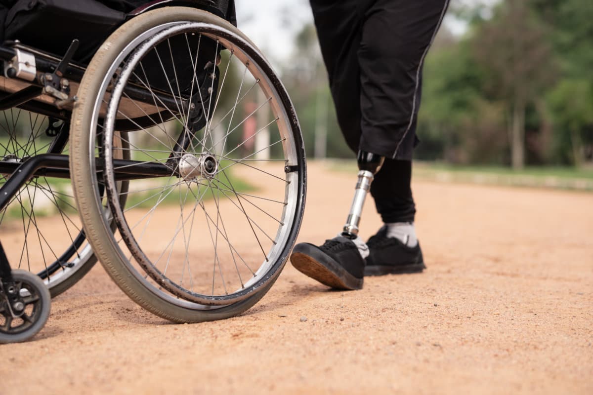 detail of man with prosthetic leg pushing wheelchair in park..