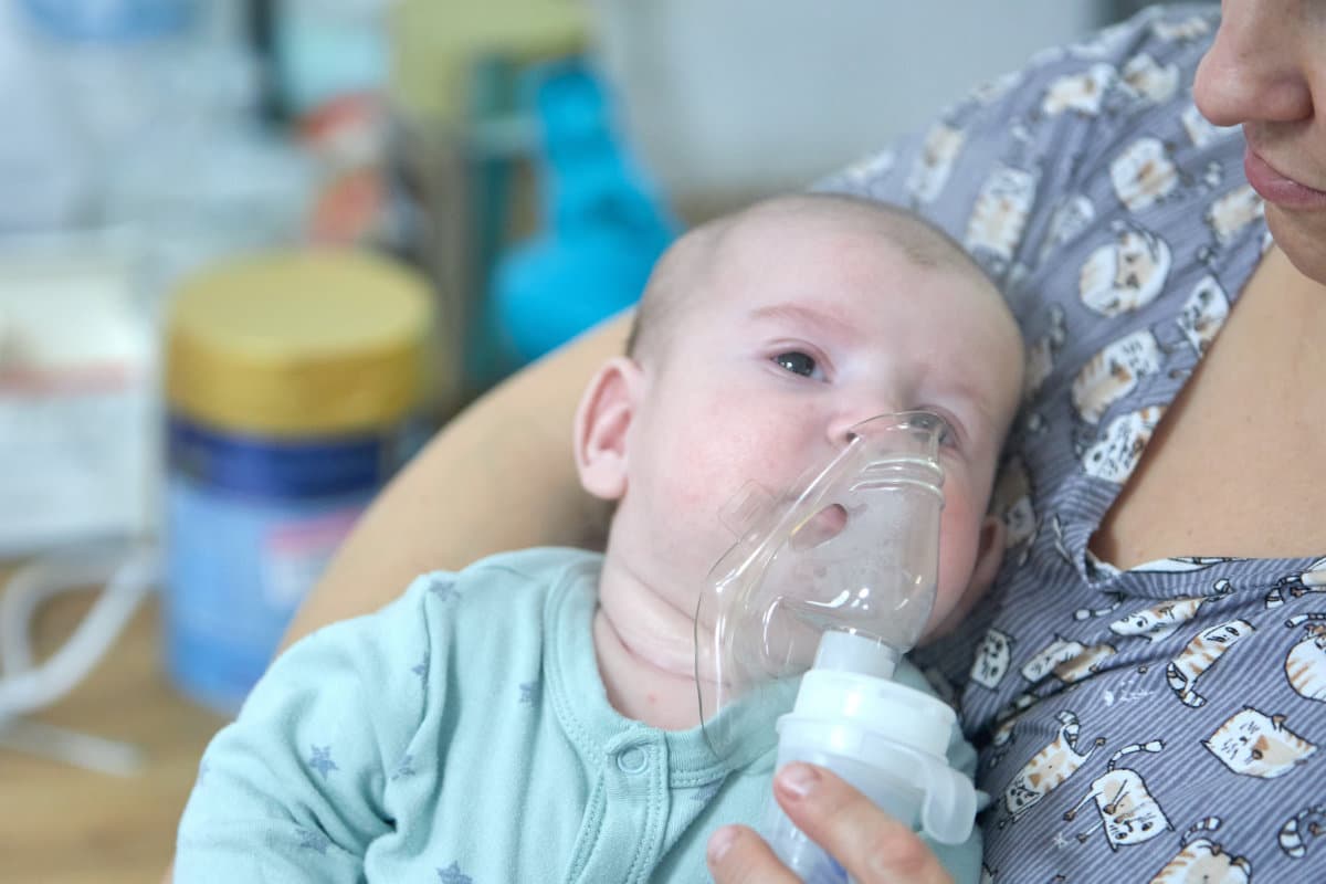 A sick child breathes with a nebulizer mask with a steam inhaler due to a respiratory disease. A mother holding an inhaler in her hands.