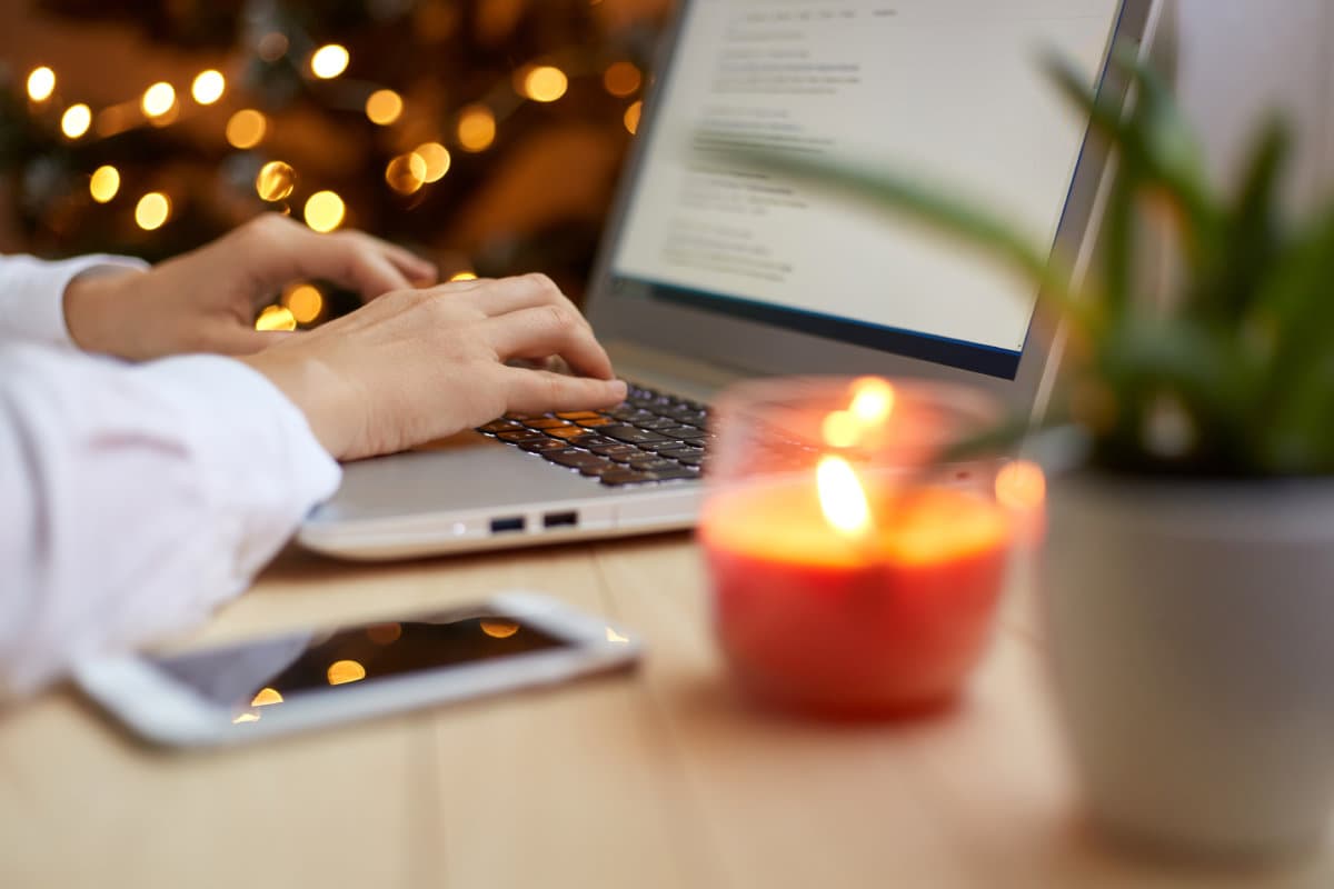 Portrait of unknown faceless woman typing on laptop keyboard while working in office interior decorated for Christmas holidays, posing near xmas tree.