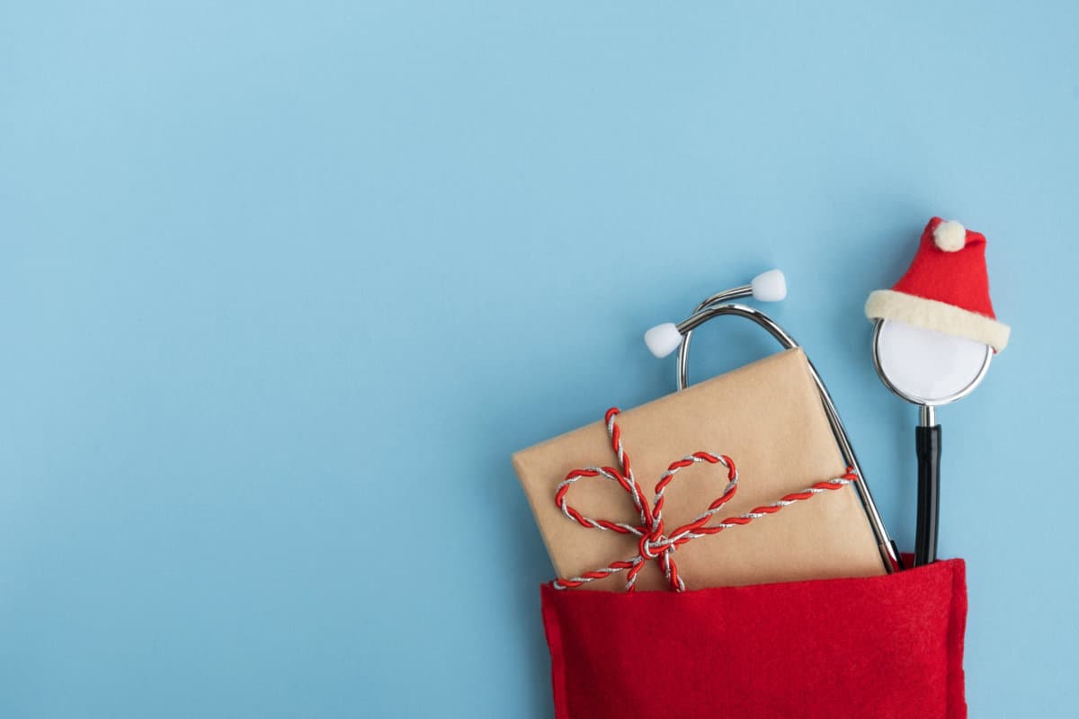 Medical stethoscope wearing hat with gift box in Santa Claus red bag. Christmas and New Year concept. Creative medical winter greeting card. Top view, flat lay, copy space