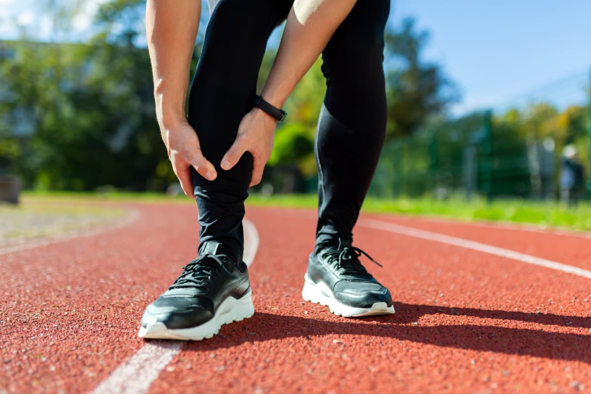 Sports injury, close-up photo of male runner&#8217;s legs, athlete injured himself while running in stadium, during fitness class, massages leg muscles