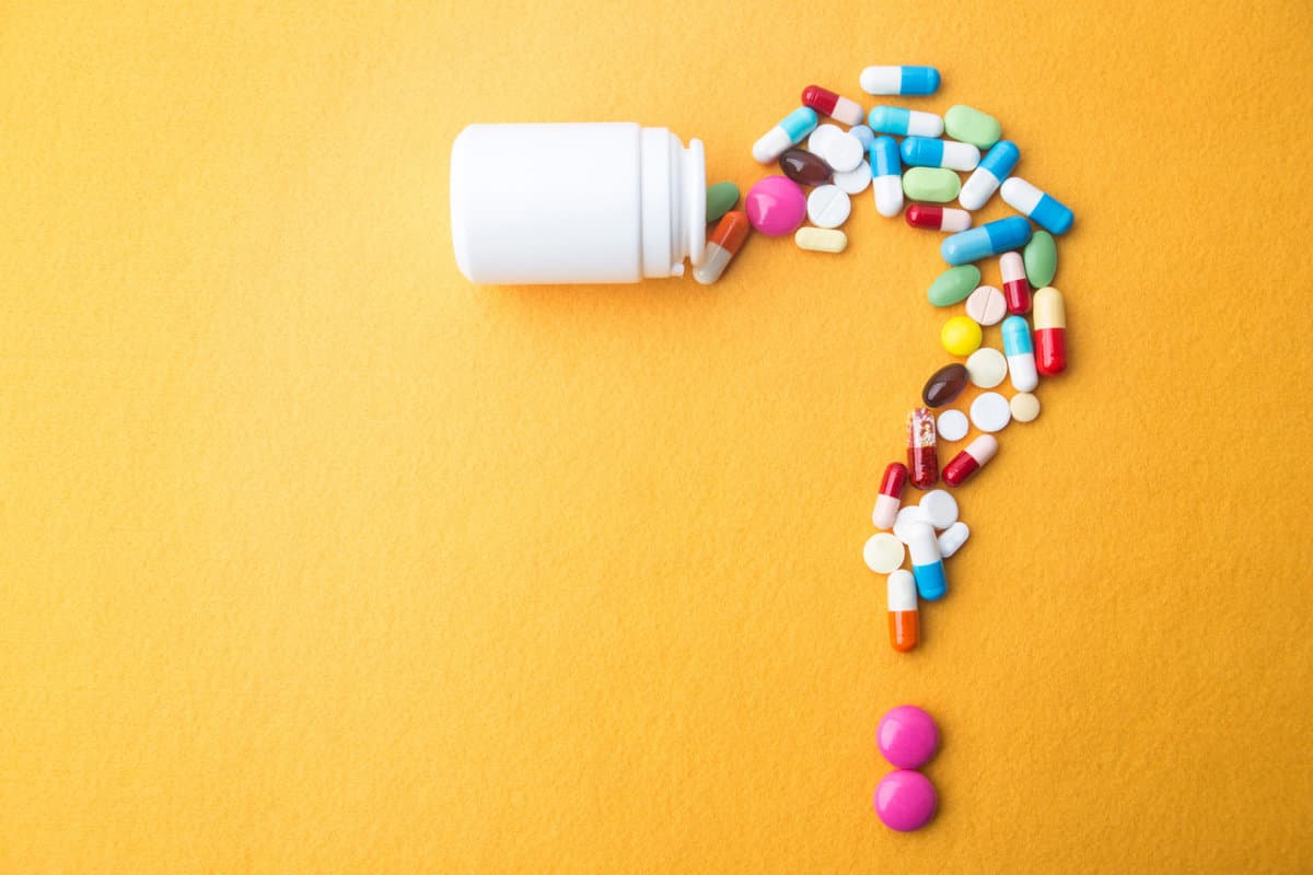 Pills or capsules as a question mark and white plastic bottle.