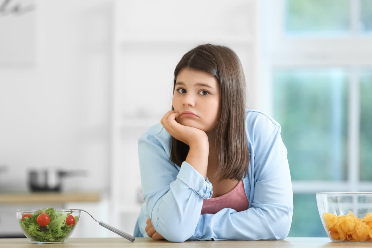 Sad overweight girl with healthy and unhealthy food in kitchen