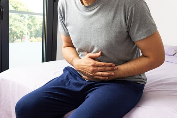 Mann sitzt mit Bauchkrämpfen auf dem Bett