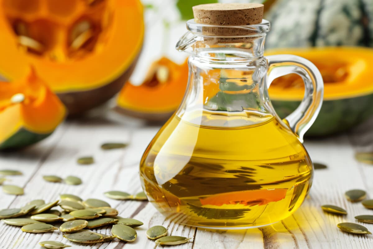 Fresh pumpkin seed oil in glass pitcher on white wooden table