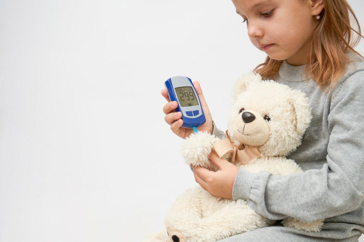Kinder- und Diabeteskonzept mit einem kleinen Mädchen, das einen Diabetestest bei einem Spielzeugbären durchführt.