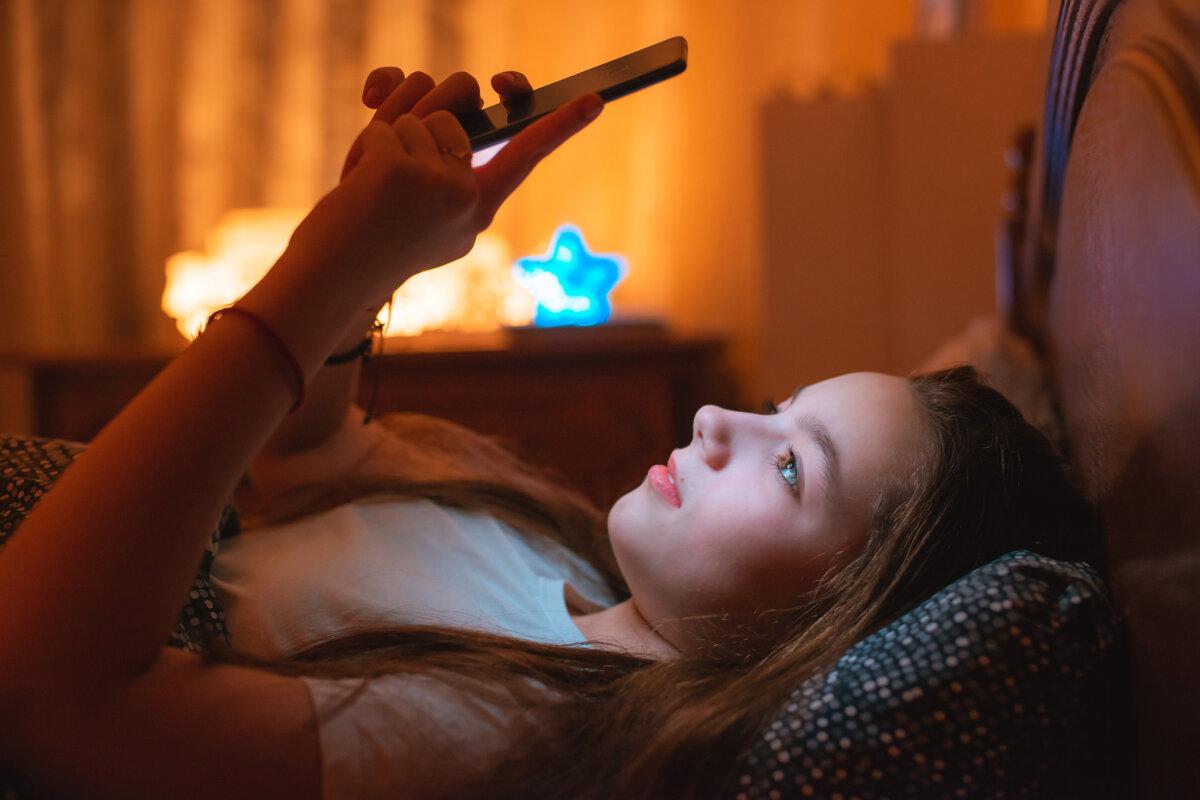 Teenager-Mädchen liegen nachts im Bett und benutzen ihr Smartphone.
