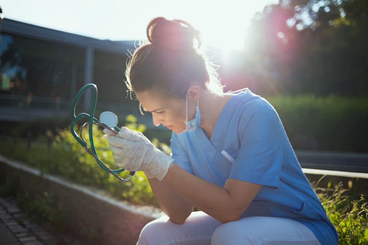 Coronavirus-Pandemie: Traurige moderne Ärztin in Uniform mit Stethoskop und medizinischer Maske, die draußen in der Nähe