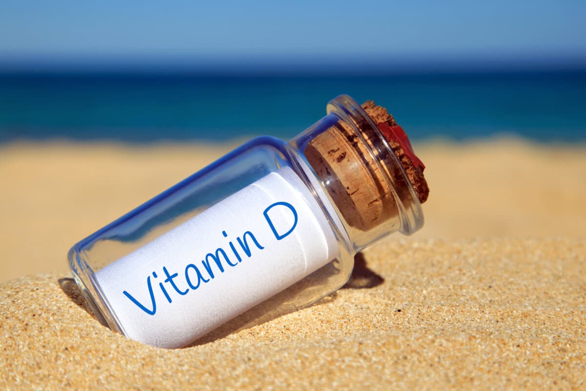 Auf einem Strand liegende, verkorkte Flasche mit einer mit "Vitamin D" beschrifteten Papierrolle.