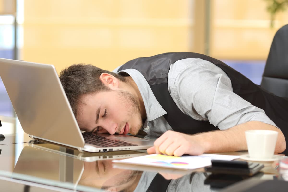 Müder, überarbeiteter Geschäftsmann schläft bei der Arbeit in seinem Büro über einem Laptop auf einem Schreibtisch