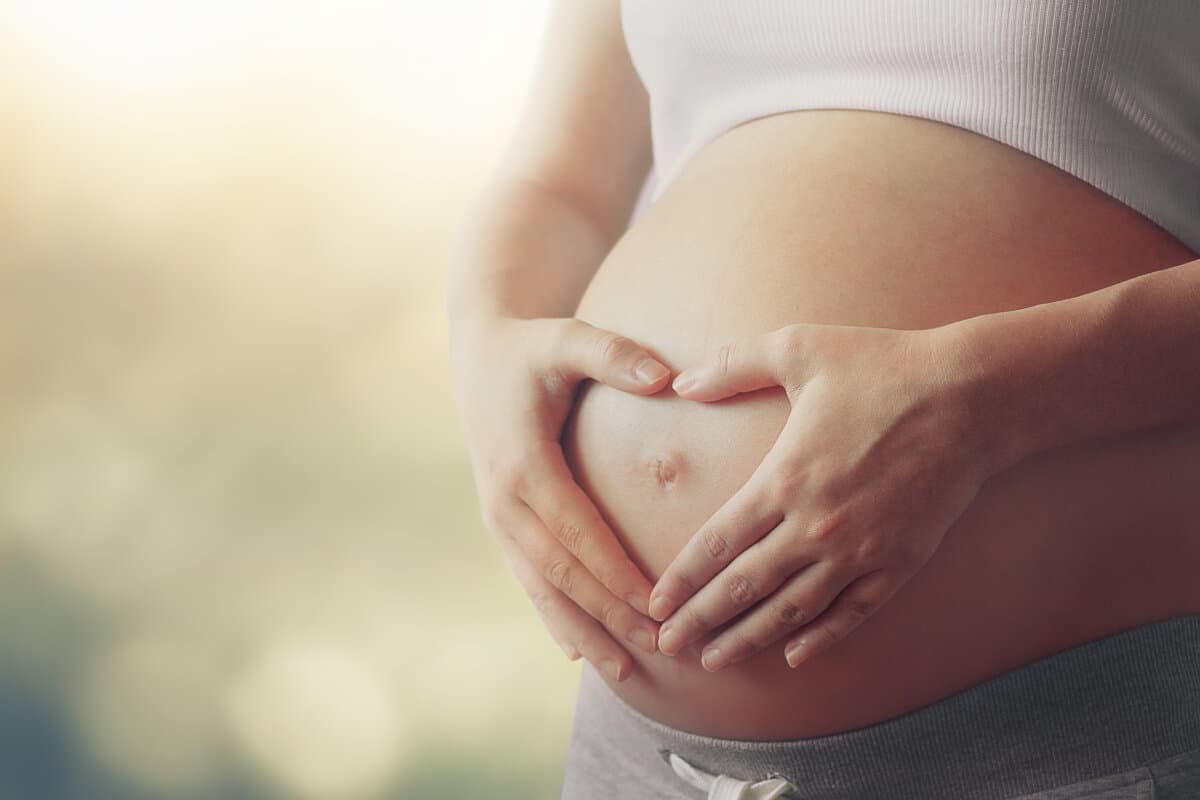 Bauch der schwangeren Frau mit Fingern Herzsymbol