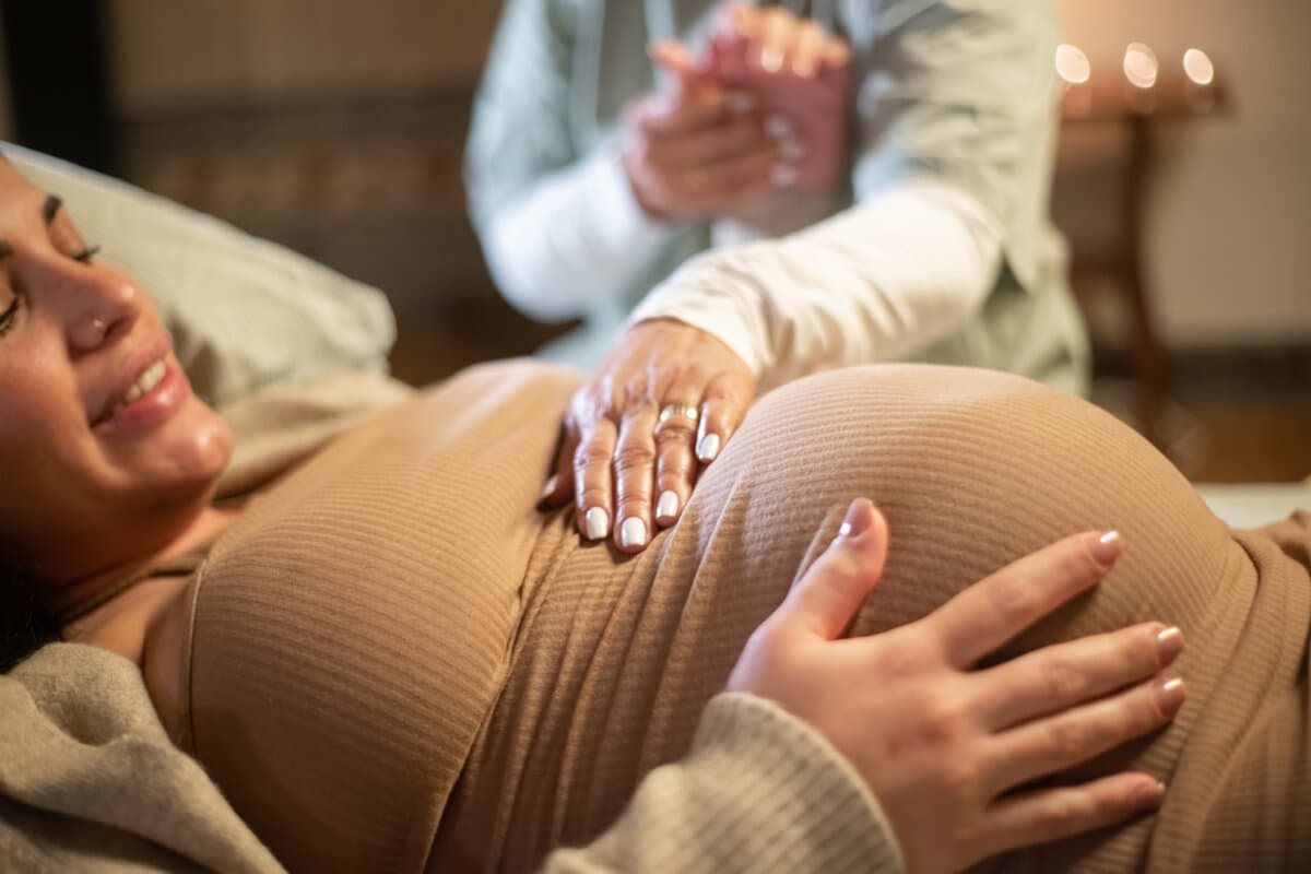 Abgeschnittenes Bild einer lächelnden schwangeren Frau und ihrer Hebamme zu Hause