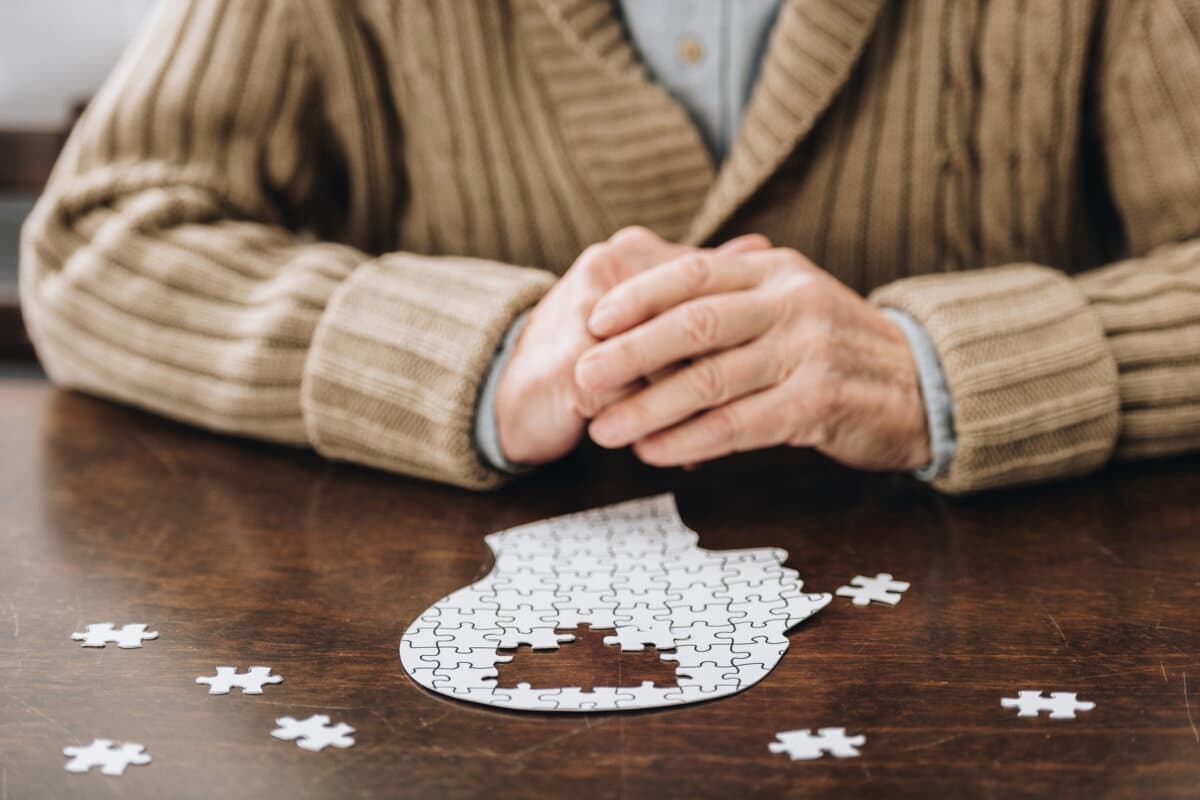 Ausgeschnittene Ansicht eines älteren Mannes, der mit Puzzles auf dem Tisch spielt