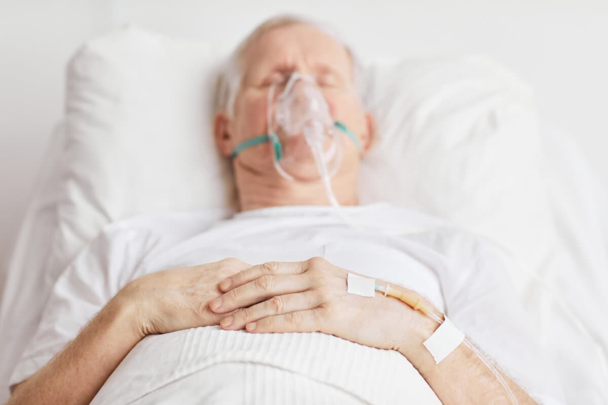 Nahaufnahme eines kranken älteren Mannes, der im Krankenhausbett liegt und sich auf die Infusionsnadel in der Hand