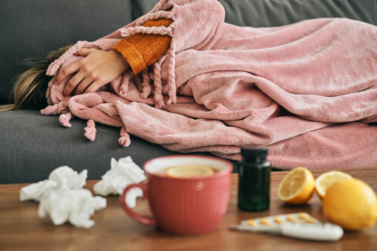 Erschöpfte kranke Frau liegt auf dem Sofa und bedeckt ihre Augen