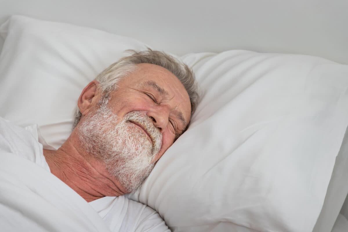 Älterer Mann schläft friedlich mit weißer Decke im Schlafzimmer