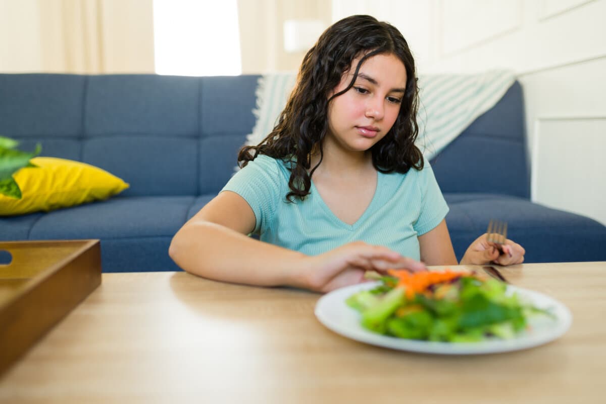 Teenager-Mädchen mit Essstörung und gesundheitlichen Problemen lehnt frischen Salat beim Mittagessen zu Hause ab