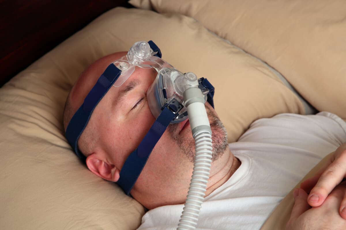 Kaukasischer Mann mit Schlafapnoe, der im Bett ein CPAP-Gerät verwendet.