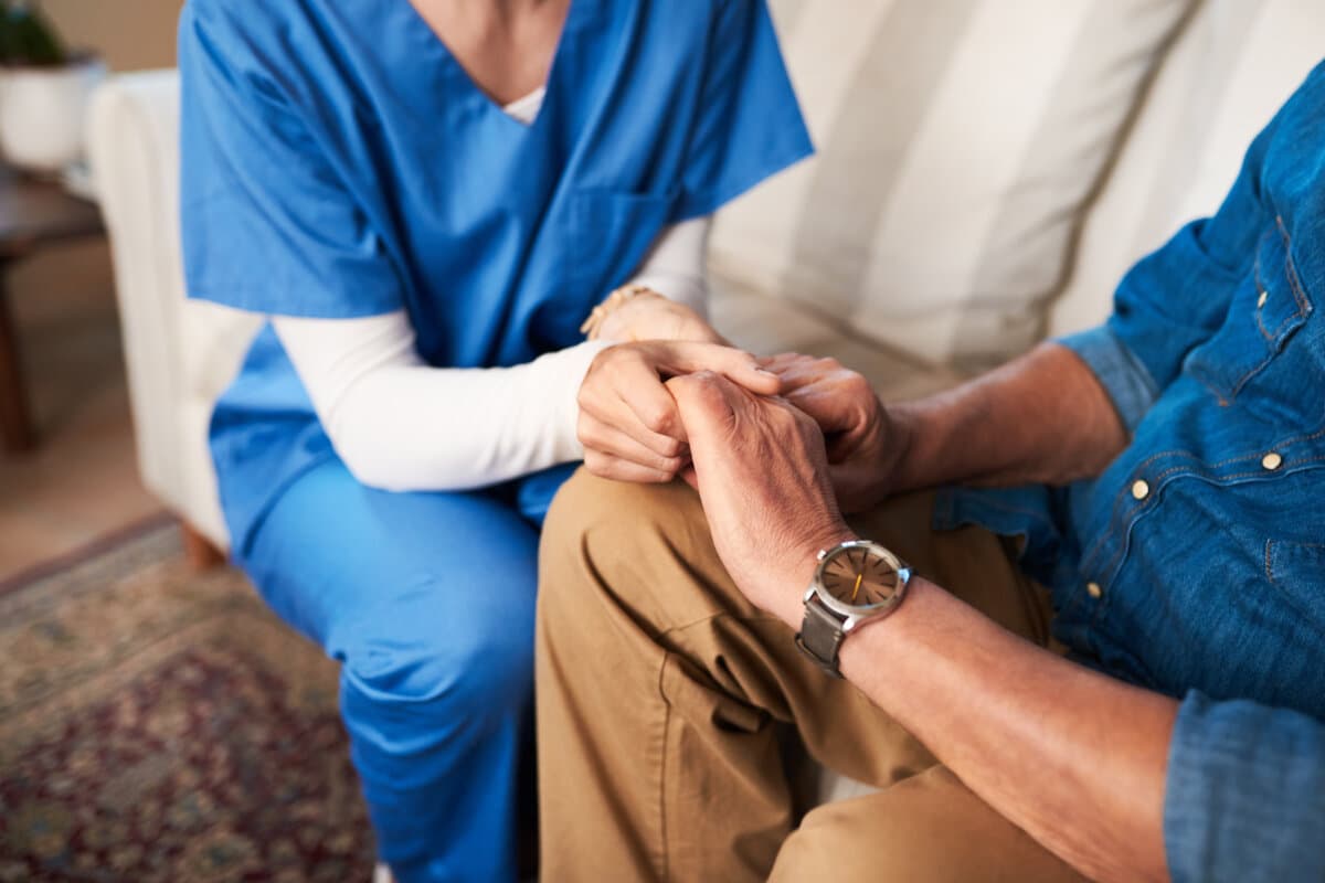 Händchenhalten, Krankenschwester und Nahaufnahme zu Hause für Unterstützung, Empathie und Palliativpflege im