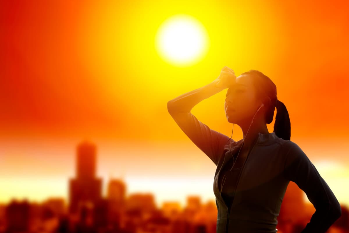 Frau schützt ihre Augen vor der Sonne bei sommerlicher Hitzewelle im Hintergrund der Stadt