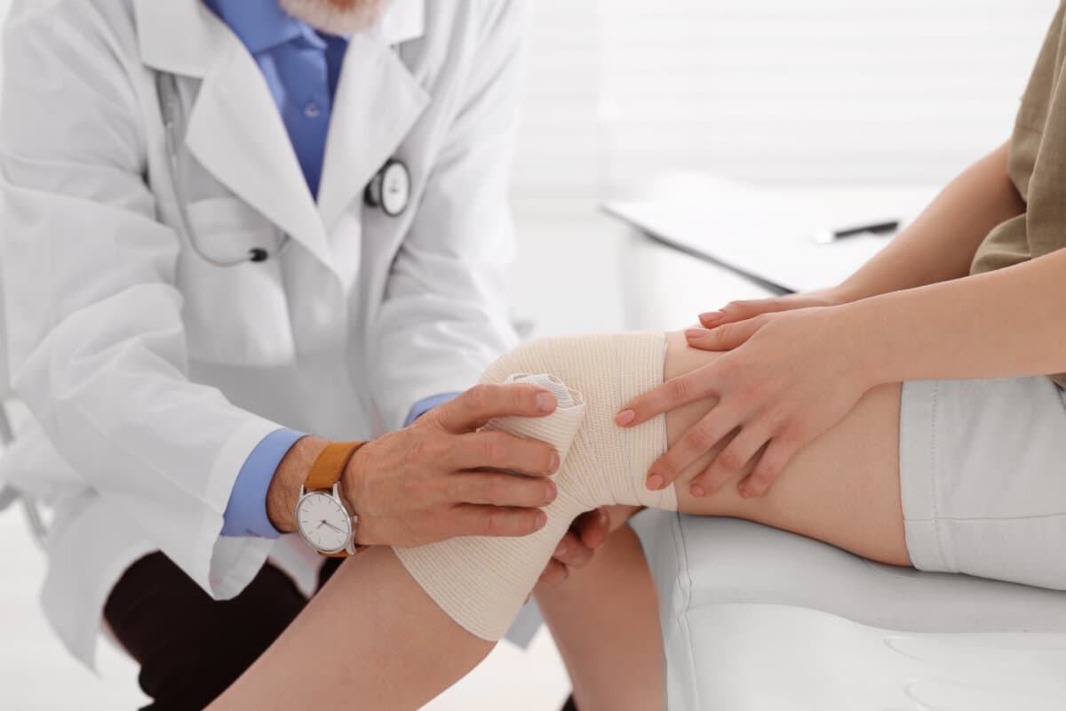 Orthopäde legt in der Klinik einen Verband am Knie des Patienten an, Nahaufnahme