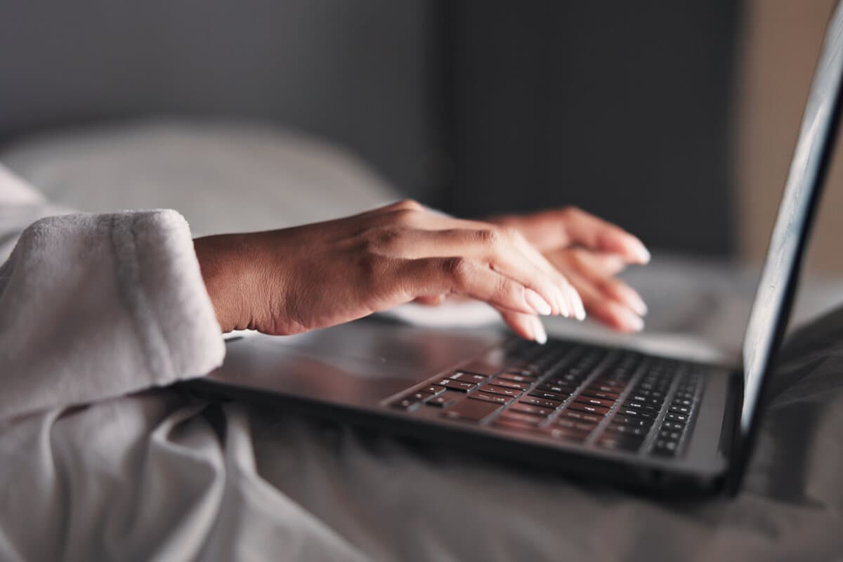 Hands, woman and laptop in bed at night for research, editing story and article submission.