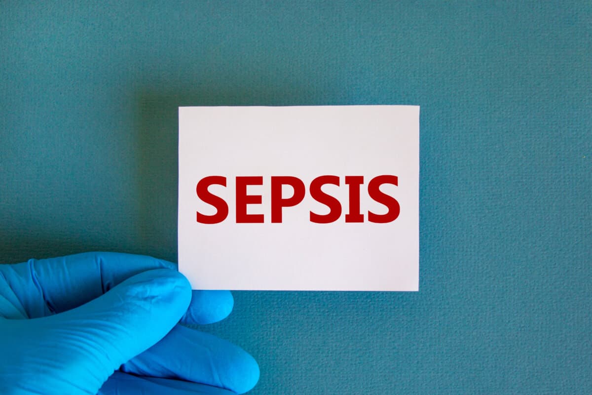 Hand in blue glove with white card. Concept word 'sepsis'. Medical concept. Copy space, beautiful blue background.