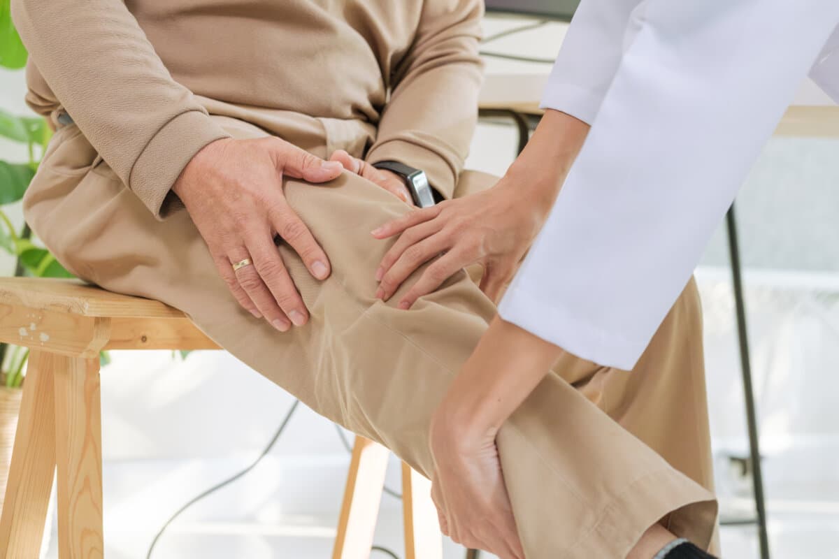 Doctor examining senior patient for osteoarthritis and knee pain during orthopedic checkup in hospital