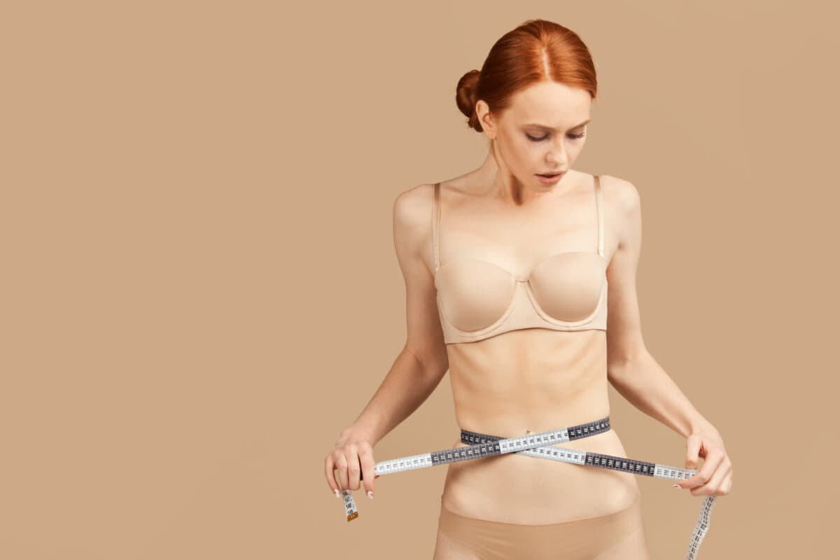 Caucasian model in underwear proud of diet results, measuring waist with tape