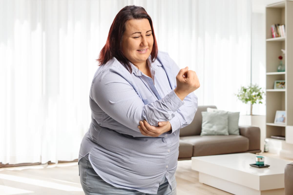 Woman in a living room standing and holding her painful elbow