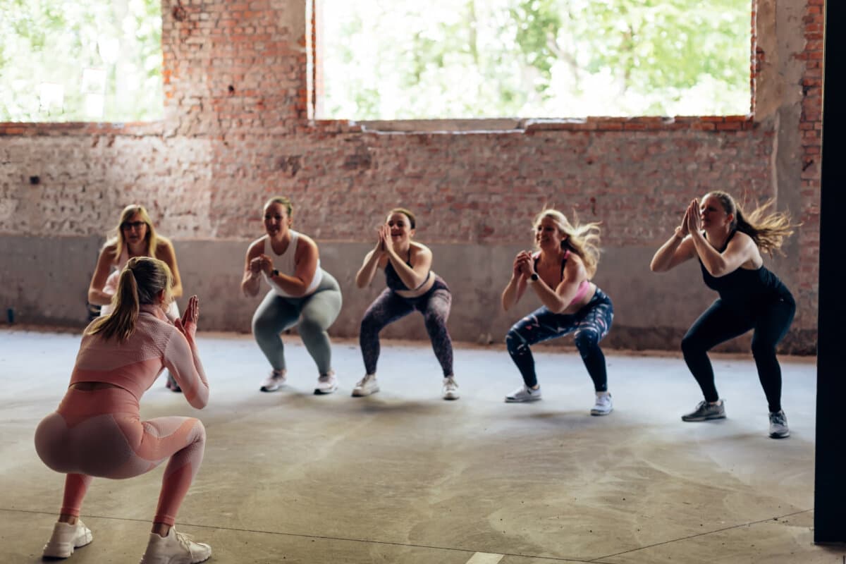 rear view of a personal trainer giving gymnastics class to a group of women with different body shapes – jumping squat