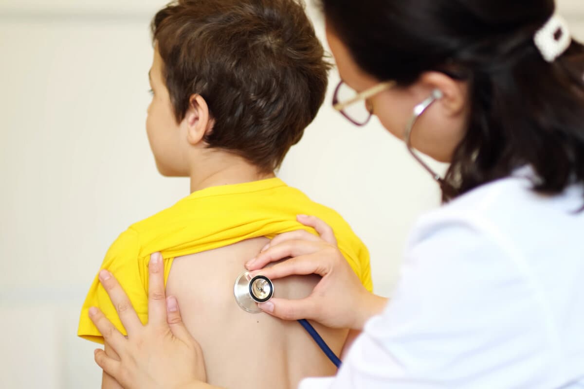 doctor listens to breath of little boy through stethoscope.