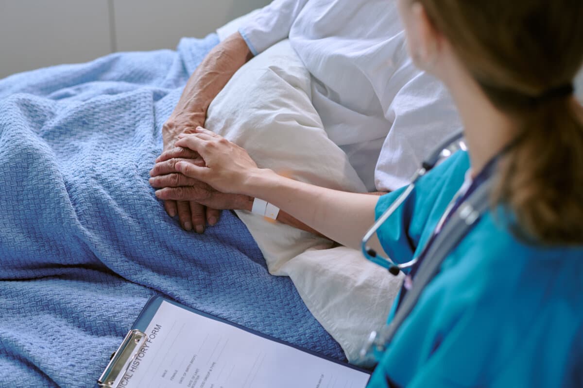 Middle Aged Female Nurse Comforting Senior Caucasian Man in Hospital Bed