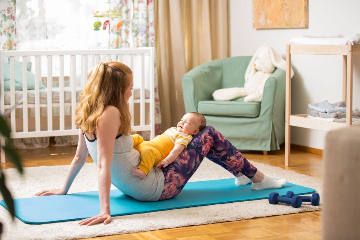 Junge Mutter trainiert gemeinsam mit ihrem Baby auf einer Yogamatte zuhause.
