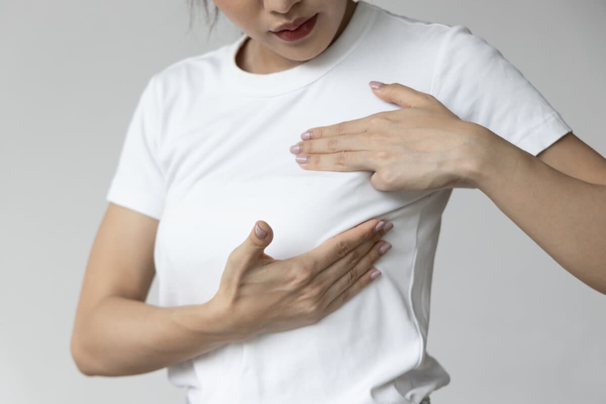 Asian woman checking her chest at home, concept of breast cancer awareness month, breast cyst or tumor inspection, body